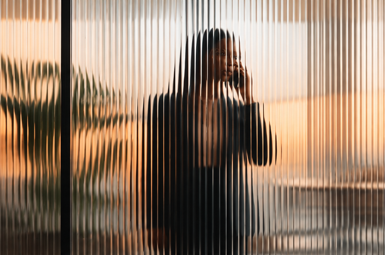 Une dirigeante au téléphone, vue à travers une cloison de verre strié, dans un bureau baigné de lumière de fin de journée.